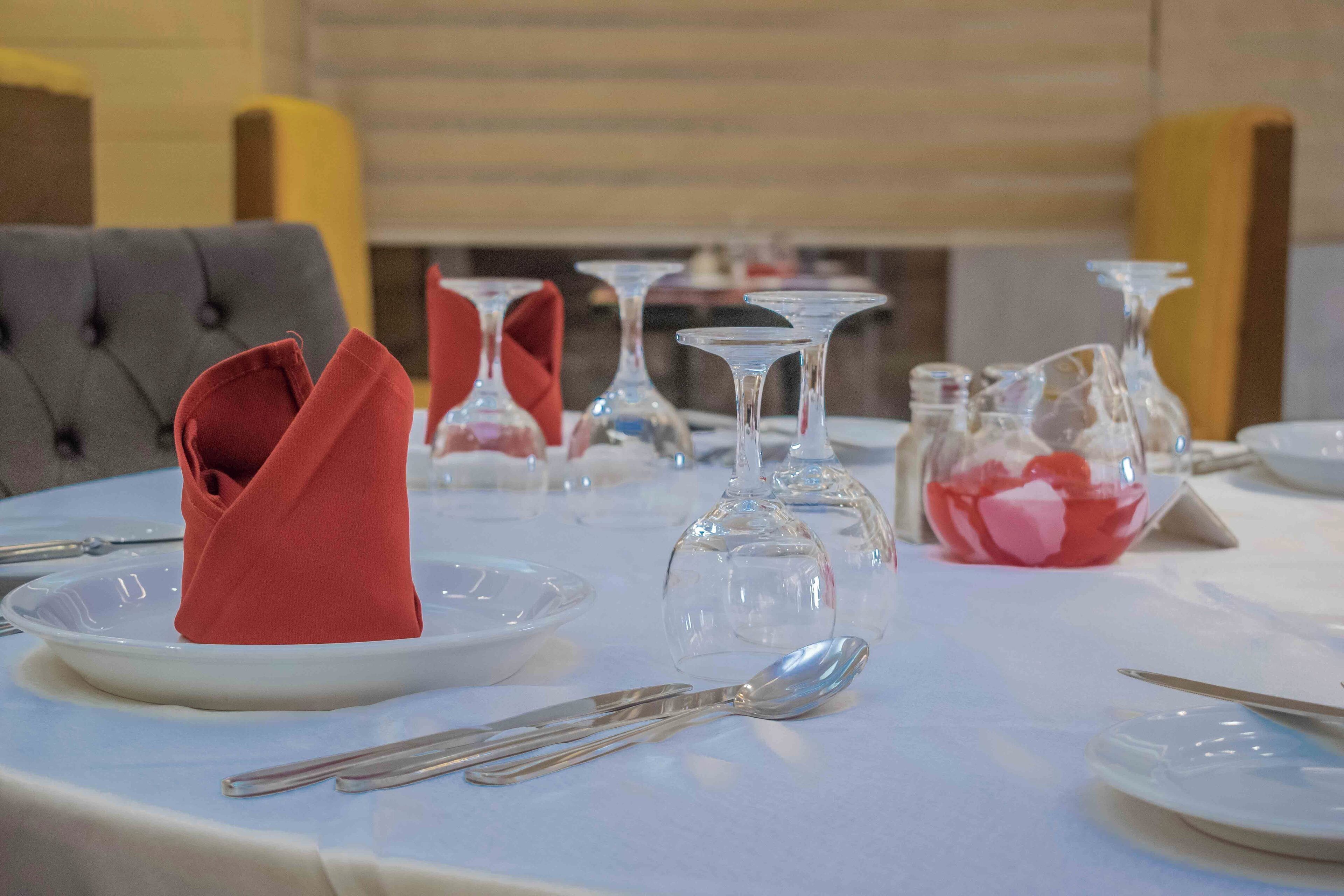 Une table à manger dressée avec des assiettes, des couverts et des verres à vin, ce qui indique une mise en place formelle pour le repas.