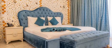 A bedroom with a tufted headboard, a matching ottoman, a bedside table with a phone, and a patterned wall.