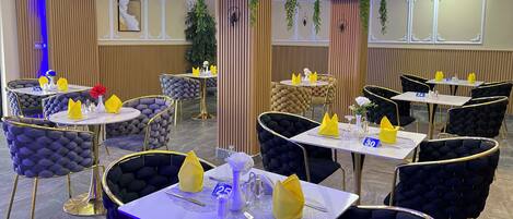 Un restaurante con mesas redondas y sillas acolchadas, cada conjunto con servilletas amarillas y un pequeño florero.