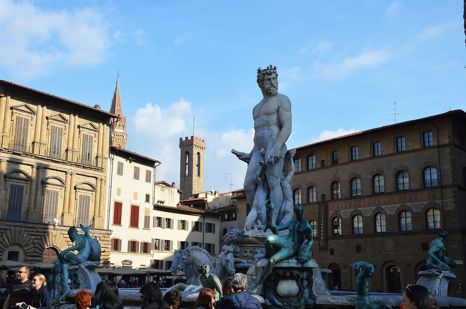 Eine Statue eines Mannes, der ein Kind trägt, umgeben von anderen Statuen, vor einem Gebäude mit einem Glockenturm.
