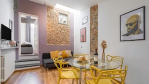 A modern living room with a stone accent wall, a glass dining table with yellow chairs, a grey sofa with yellow cushions, and a mounted TV. - Elevator, Ac, Wifi - Heart of historic city center (Florence)