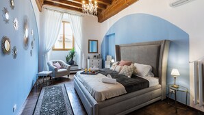 A bedroom with a large bed, a chair, a dresser, and a chandelier. - A Florence Palace - 4 Bedroom Apt - Santa Croce (Florence)
