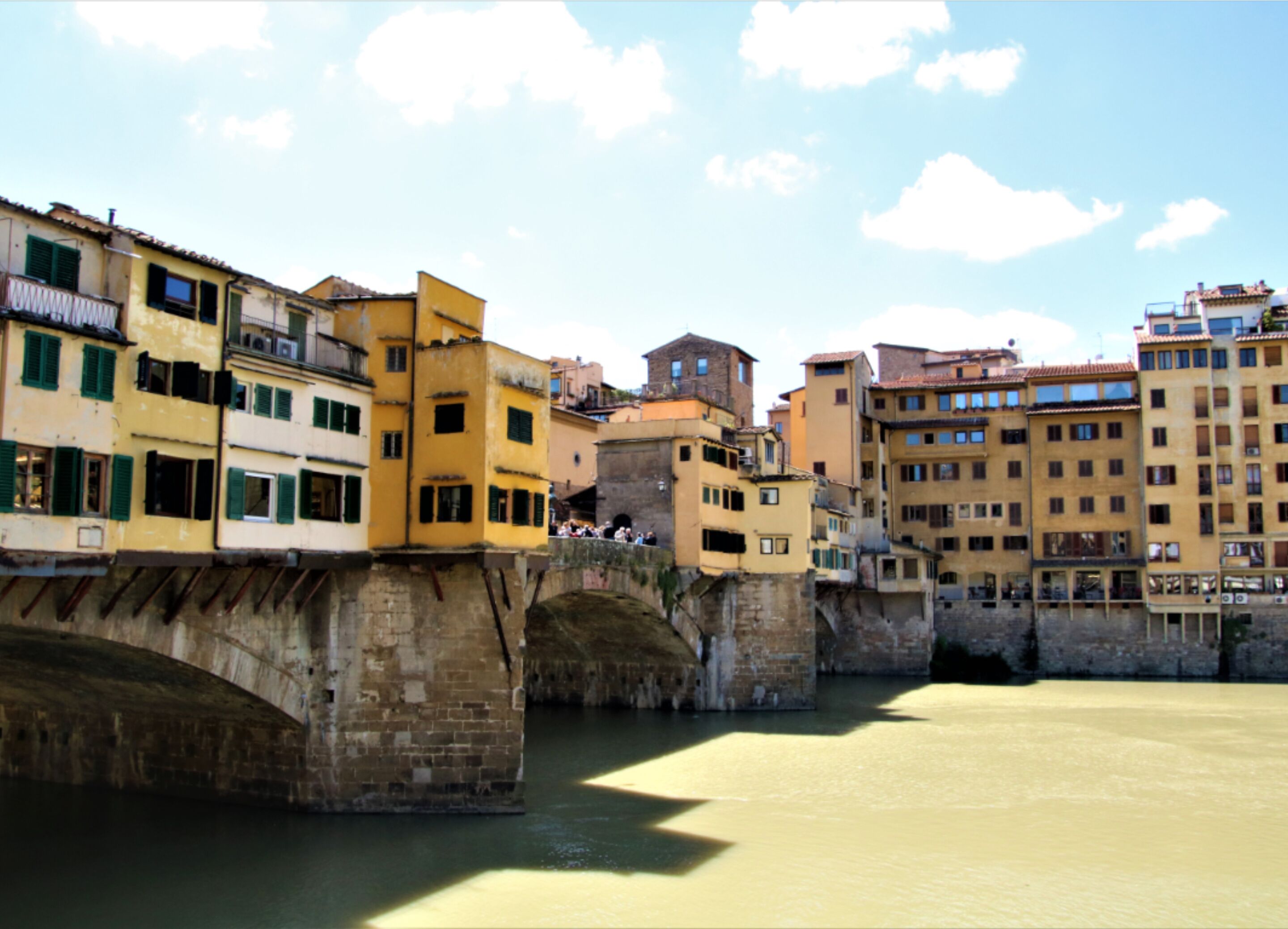 A historic bridge with buildings on either side, a river below, and a clear sky.