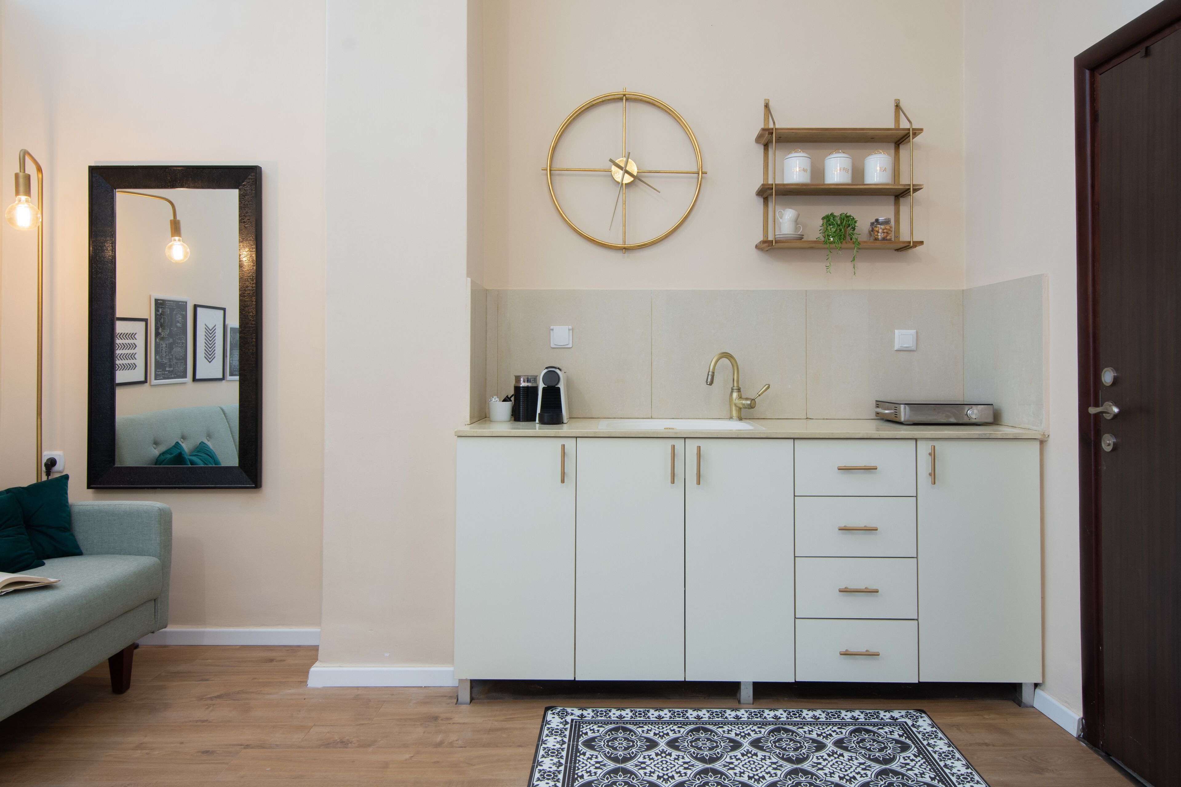Una cocina moderna con encimera blanca, un reloj con marco dorado y una estantería de madera con frascos.