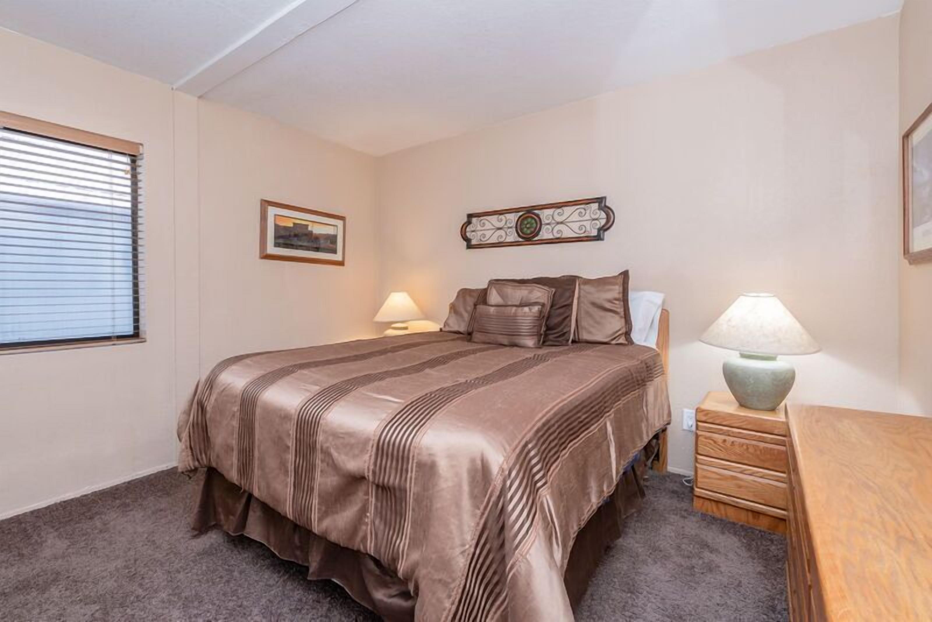 Une chambre à coucher avec un grand lit, deux lampes de chevet, une table de nuit en bois et un tableau encadré au mur.