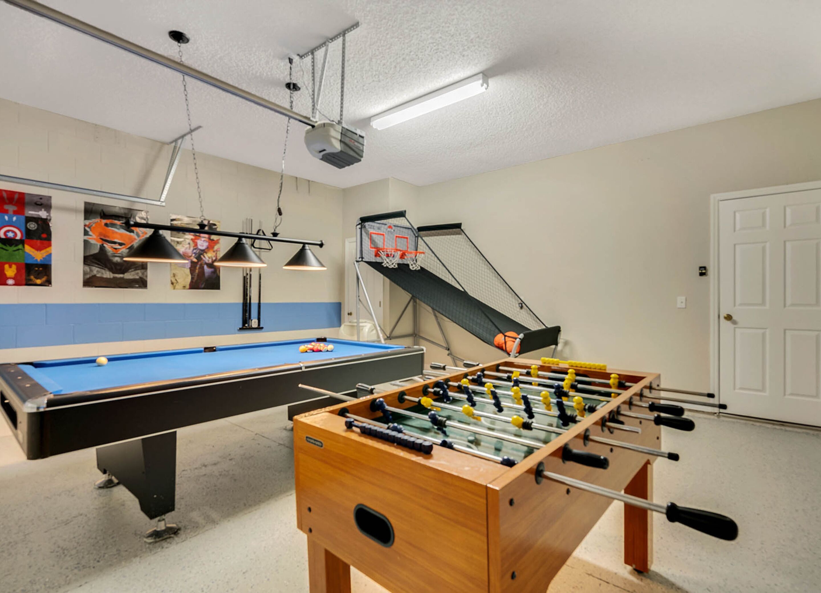 A room with a pool table, a foosball table, a basketball hoop, and a ceiling-mounted projector.