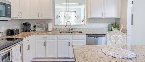A modern kitchen with white cabinetry, granite countertops, stainless steel appliances, and a central island with a decorative wheel.