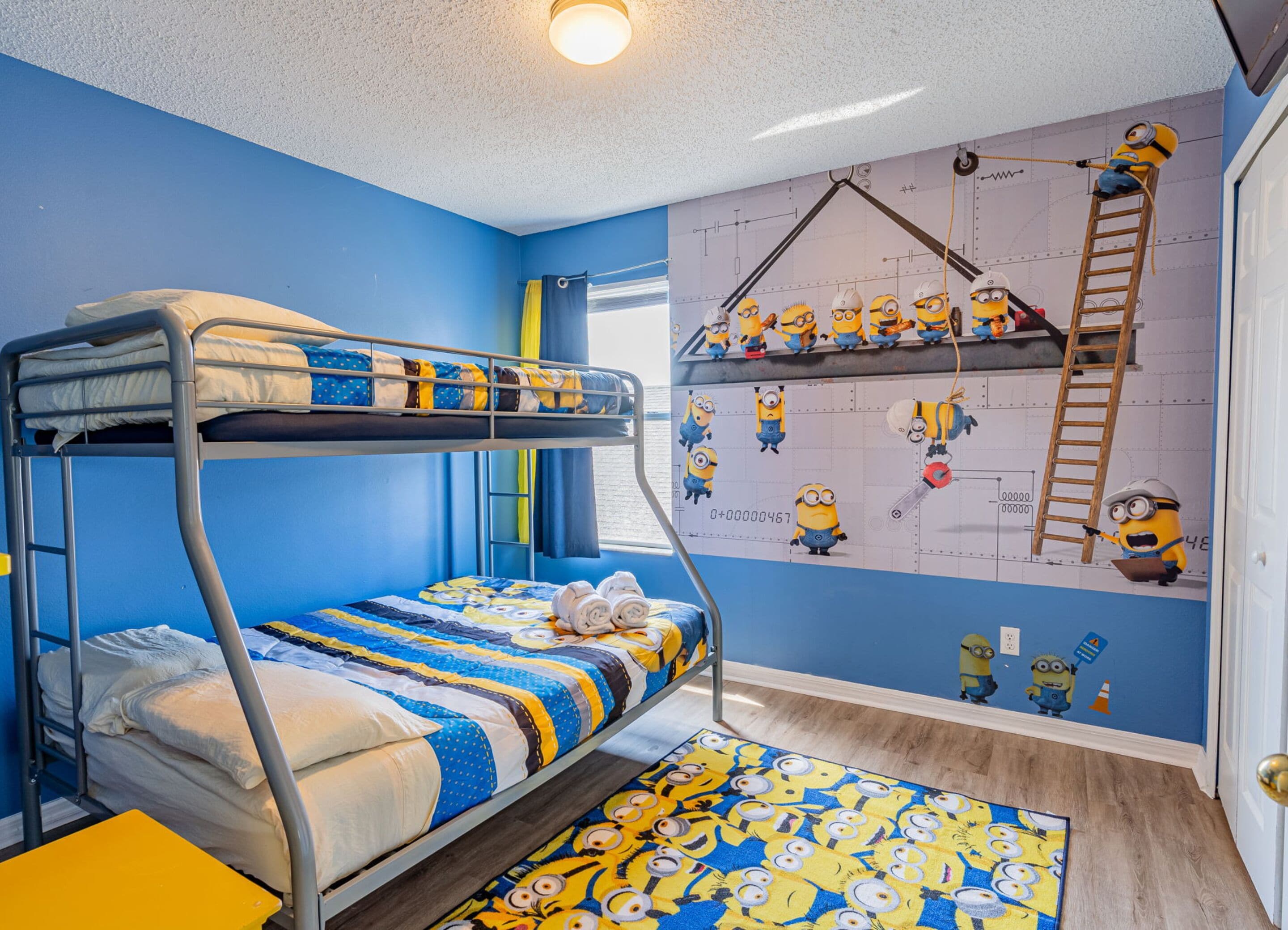 Et soveværelse med køjesenge, et vægmaleri med Minion-tema, et vindue med gardiner og en gul stol.