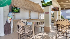 An outdoor bar area with wicker chairs, a thatched roof, and a television screen. - 4 Bedroom Townhouse, Resort, 15 Mins to Disney, Themed Rooms perfect for Kids (Kissimmee)