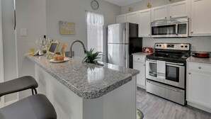 A modern kitchen with white cabinets, stainless steel appliances, granite countertops, and a built-in island with seating. - 4 Bedroom Townhouse, Resort, 15 Mins to Disney, Themed Rooms perfect for Kids (Kissimmee)