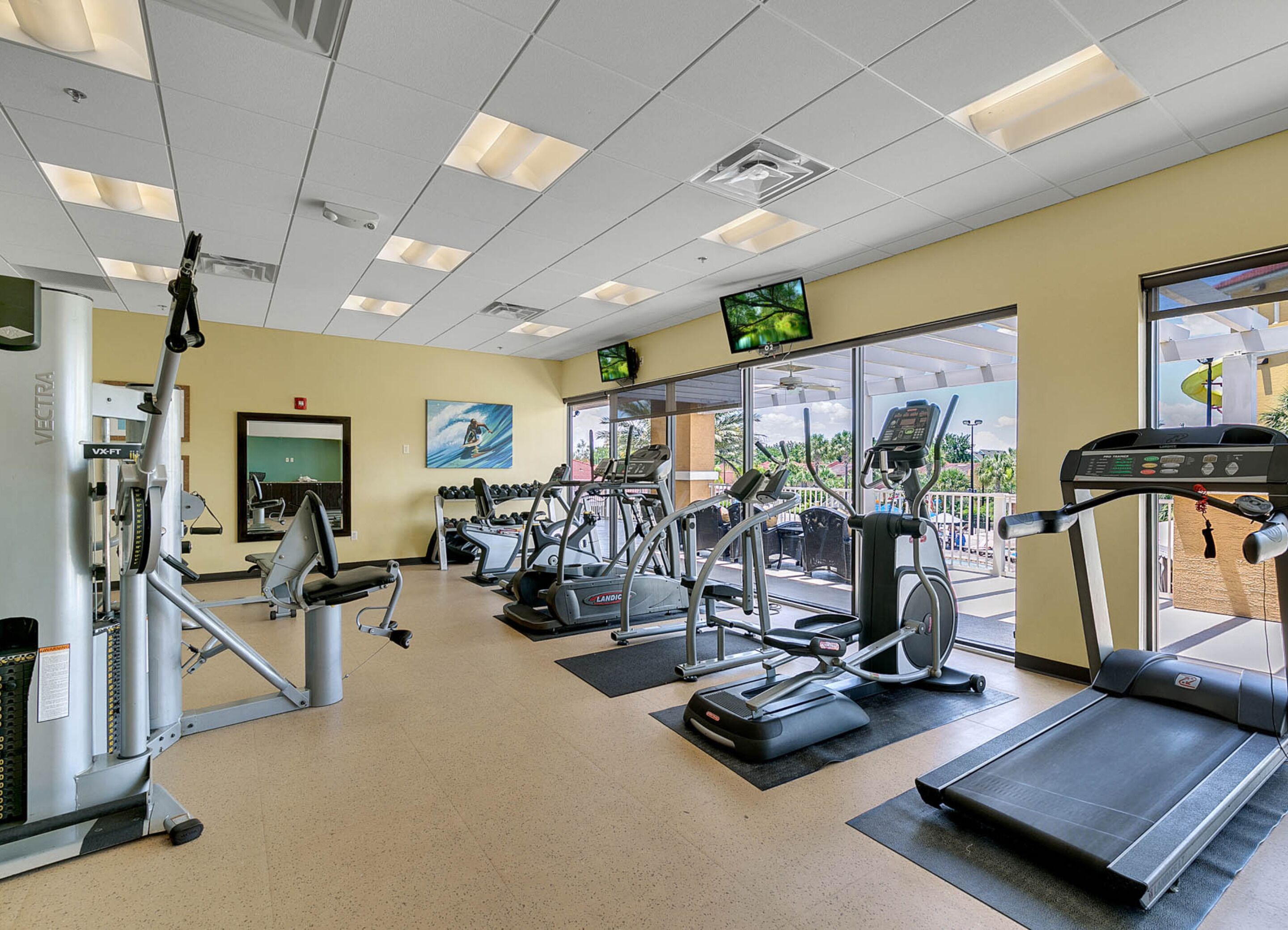 A gym with cardio machines, weight machines, and a TV screen.