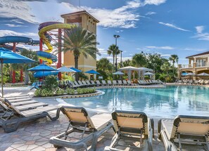 A pool area with lounge chairs, umbrellas, and a water slide structure.