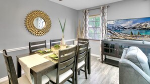 Comedor con una mesa dispuesta para cuatro, ventilador de techo, espejo decorativo y vistas panorámicas a través de una ventana.