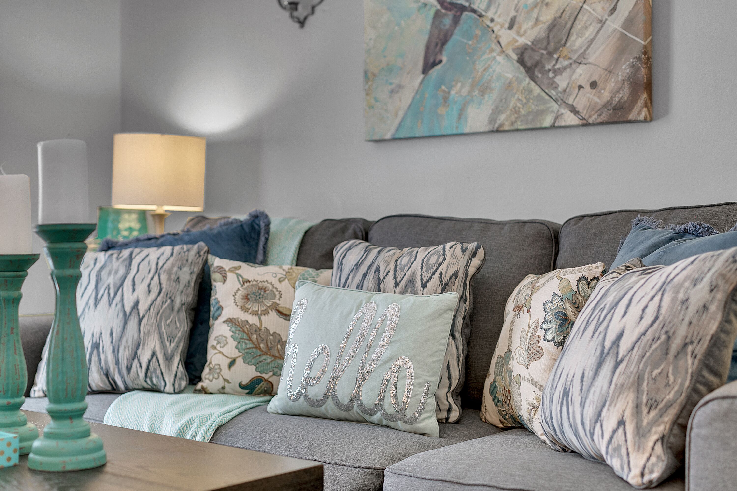 A grey sofa with multiple decorative pillows, a teal vase, and a wall-mounted lamp.