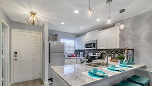 A modern kitchen with white cabinets, granite countertops, and teal bar stools. - Family Vacation Home, Water Park+Endless Amenities (Kissimmee)