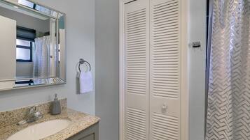 A bathroom with a granite countertop sink, a mirror, a towel rack, and a white closet with louvered doors.