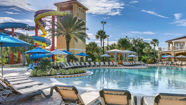 A pool area with lounge chairs, umbrellas, and a water slide structure. - Family Vacation Home, Water Park+Endless Amenities (Kissimmee)