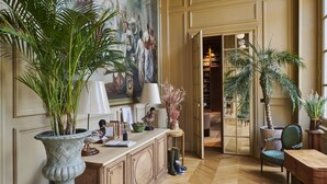 Une pièce spacieuse, ornée d’un grand tableau, d’un bureau en bois, d’une chaise et de plusieurs plantes en pot.