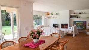 A dining area with a wooden table, chairs, and a vase of flowers. There is a bed with a white cover in the background, and a TV on a stand. - Villa 100 meters from the sea, in the Platja de Pals Golf Club. A/C (Pals)