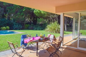 An outdoor patio with a table set for dining, surrounded by chairs, and a glass door leading to a garden. - Villa 100 meters from the sea, in the Platja de Pals Golf Club. A/C (Pals)