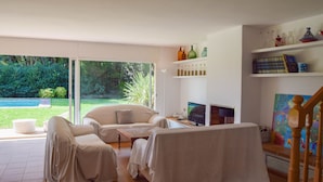 A spacious living room with a large sliding glass door leading to a garden, a comfortable sofa, a coffee table, and a television. - Villa 100 meters from the sea, in the Platja de Pals Golf Club. A/C (Pals)
