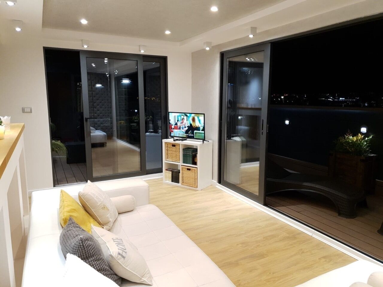 Una sala de estar moderna con un sofá blanco, un televisor de pantalla plana y un ventanal corredero que da a un espacio exterior.