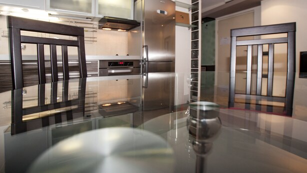 A modern kitchen with a glass-top table, stainless steel appliances, and a wooden chair. - Metropol (Belgrade)