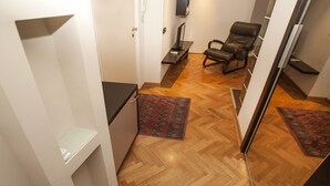 A hallway with wooden flooring, a black leather chair, and a small shelf unit. - Metropol (Belgrade)