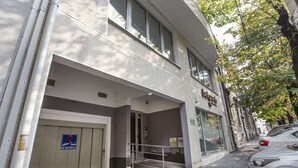 A building with a garage door, a staircase leading to an entrance, and parked cars along the street.