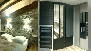 A bedroom with a stone wall, wooden beams, a bed with white bedding, and a sliding door leading to a bathroom. - New apartment 8 people in chalet in Champagny / La Plagne (Champagny-en-Vanoise)