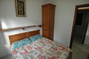 Una camera da letto con un letto in legno, una coperta a motivi decorativi, un armadio in legno e una porta che dà su un'altra stanza.