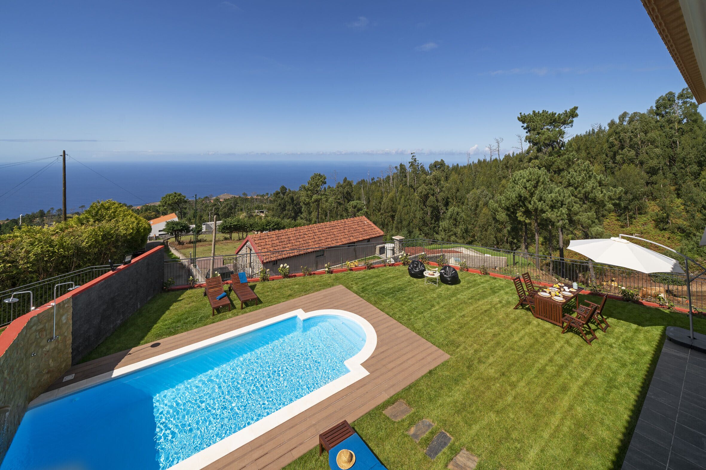 Un patio trasero con piscina, zona de comedor y vista al océano.