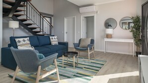 A modern living room with a blue sofa, two armchairs, a coffee table, a staircase, and a white console table with a mirror and plant. - Felicidade Rocha II - For families, with a pool (Ponta do Pargo)