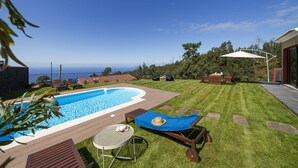 A backyard with a swimming pool, lounge chairs, a table, and a view of the ocean. - Felicidade Rocha II - For families, with a pool (Ponta do Pargo)