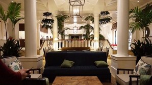 Um lobby com um sofá azul escuro, uma mesa de centro de madeira e duas cadeiras com almofadas florais.