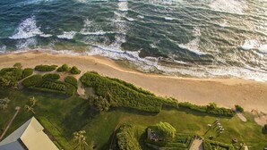 Vista aérea de uma praia com gramado bem cuidado e uma estrutura com telhado triangular.