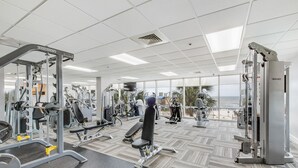 A gym with various exercise machines, large windows, and a view of the beach. - Gulf Shores condo with fabulous views of the Gulf of America (Gulf Shores)