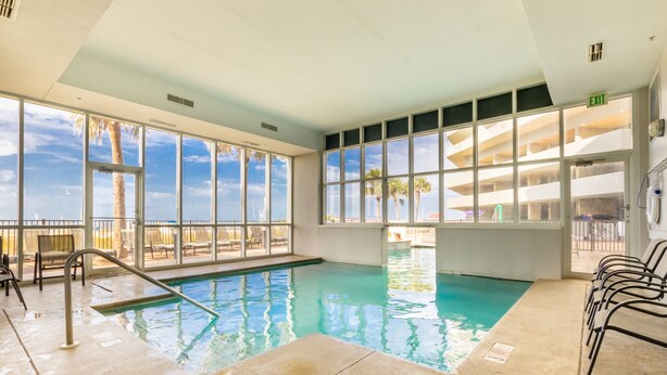 An indoor swimming pool with clear views of palm trees and a building outside. - Gulf Shores condo with fabulous views of the Gulf of America (Gulf Shores)