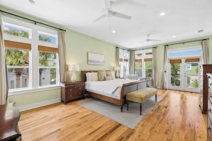 A bedroom with a bed, bedside tables, a bench, a ceiling fan, and large windows with curtains.