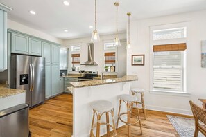 A modern kitchen with stainless steel appliances, a central island with stools, and a dining area with a view.