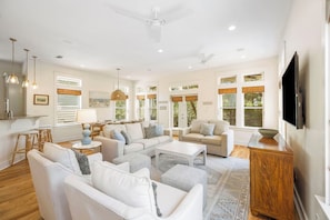 A spacious living room with white sofas, a coffee table, a TV, and a ceiling fan.
