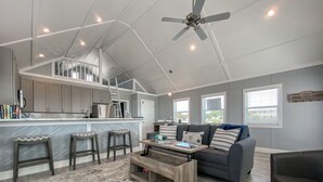 A spacious living area with a high ceiling, a kitchen with a bar, and a gray sofa with striped pillows. - BAYDREAM - Peaceful! Inviting! Clean! Floating quiet getaway! Dock your boat!! (Pensacola)