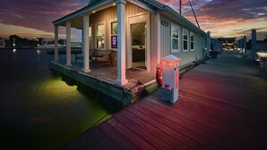 A waterfront house with a covered porch, a small deck, and a lifebuoy near the entrance. - BAYDREAM - Peaceful! Inviting! Clean! Floating quiet getaway! Dock your boat!! (Pensacola)