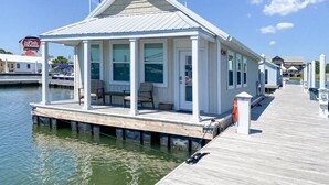 A waterfront house with a covered porch, large windows, and a dock extending into the water. - BAYDREAM - Peaceful! Inviting! Clean! Floating quiet getaway! Dock your boat!! (Pensacola)