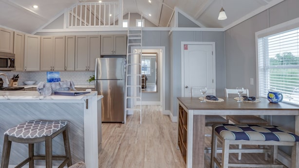A modern kitchen with a central island, a dining area with a bench, and a staircase leading to an upper level. - BAYDREAM - Peaceful! Inviting! Clean! Floating quiet getaway! Dock your boat!! (Pensacola)