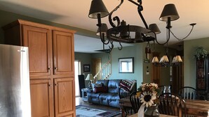 A kitchen with wooden cabinets, a stainless steel refrigerator, a dining table with chairs, and a chandelier. - WINTERFELL-NH BEST OF NH GORGEOUS LAKE &  MOUNTAIN VIEWS,  NEVER PP ADDS (Pittsburg)