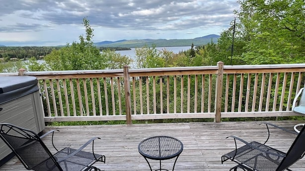 A wooden deck with two metal chairs and a small round table, overlooking a lake and mountains. - WINTERFELL-NH BEST OF NH GORGEOUS LAKE &  MOUNTAIN VIEWS,  NEVER PP ADDS (Pittsburg)