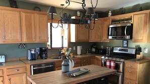 A kitchen with wooden cabinets, a central island, a stove, a microwave, and a coffee maker. - WINTERFELL-NH BEST OF NH GORGEOUS LAKE &  MOUNTAIN VIEWS,  NEVER PP ADDS (Pittsburg)