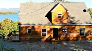 A log cabin with a front porch, a chimney, and a view of a lake. - WINTERFELL-NH BEST OF NH GORGEOUS LAKE &  MOUNTAIN VIEWS,  NEVER PP ADDS (Pittsburg)