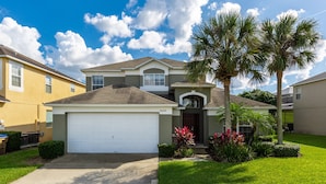 A two-story house with a white garage door, a front porch, and a well-maintained lawn with palm trees. - Mickeys Encore by VillaDirect (Kissimmee)